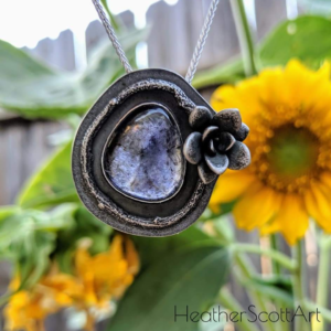 Pendant made with iolite, cast tree branch, and a succulent in front of sun flowers