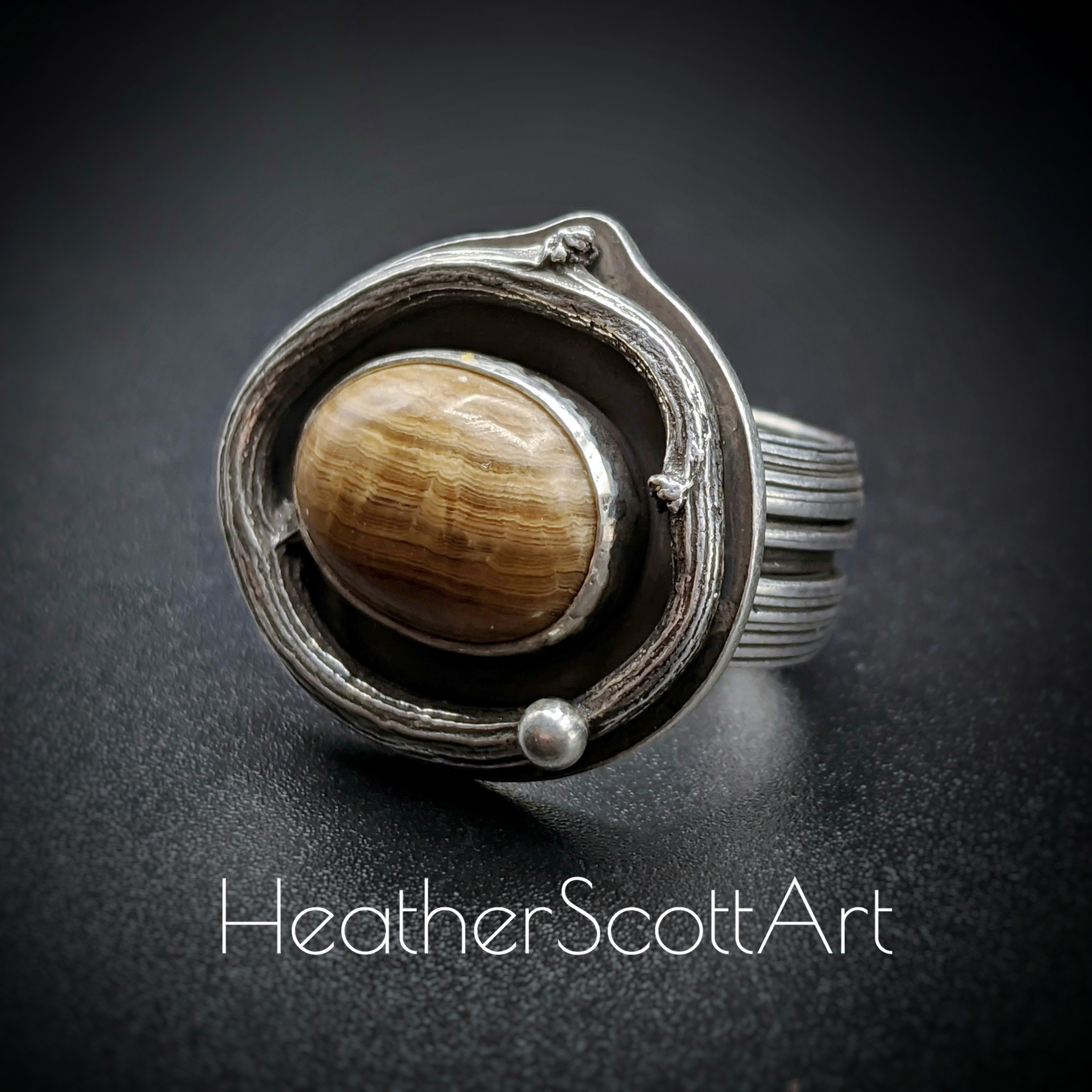 brown oval agate ring with a branch surrounding the stone and a linear textured ring band