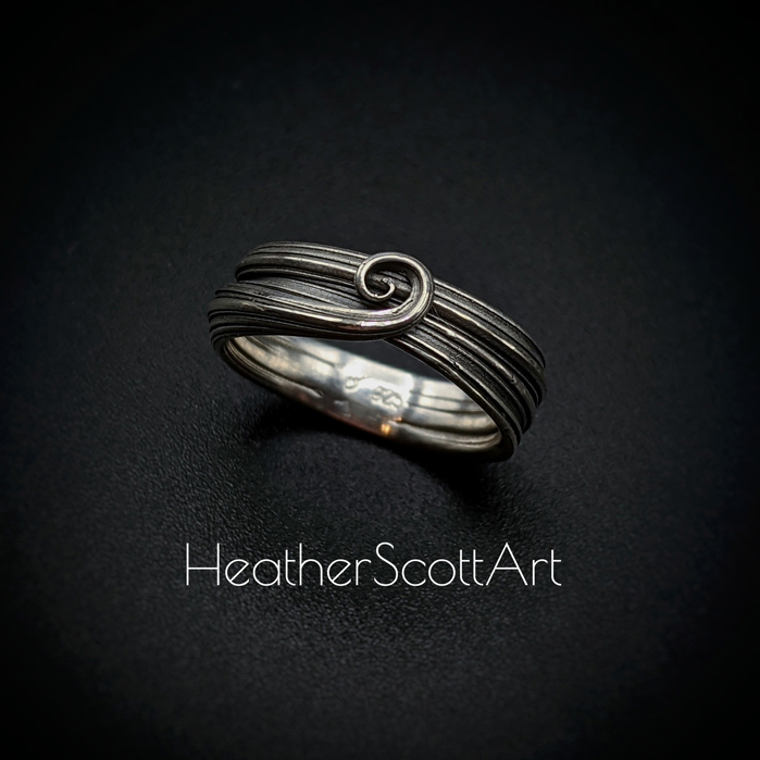 Sterling silver ring with a sculptural swirl on the front. It has a linear texture that wraps around the entire ring.