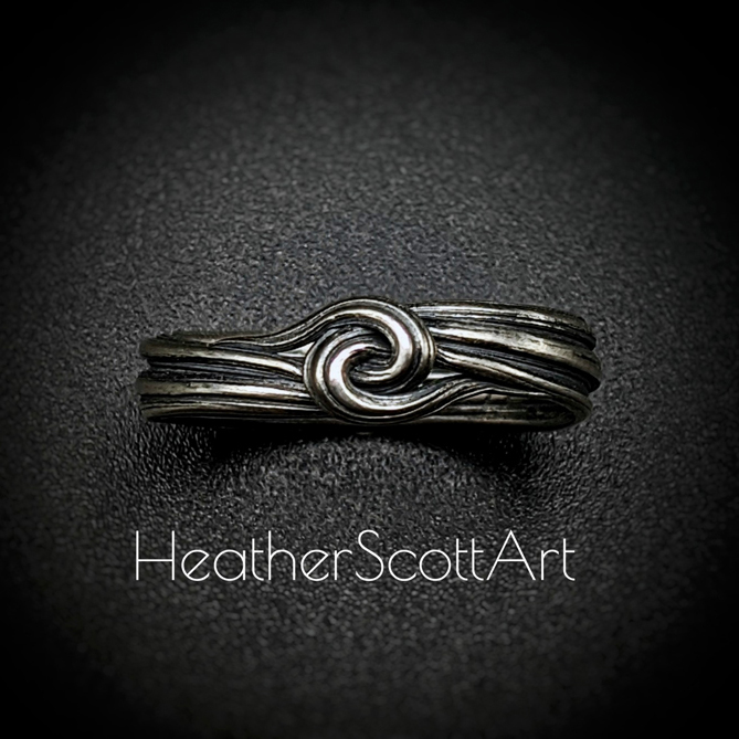 Sterling silver ring with a sculptural knot on the front. It has a linear texture that wraps around the entire ring.