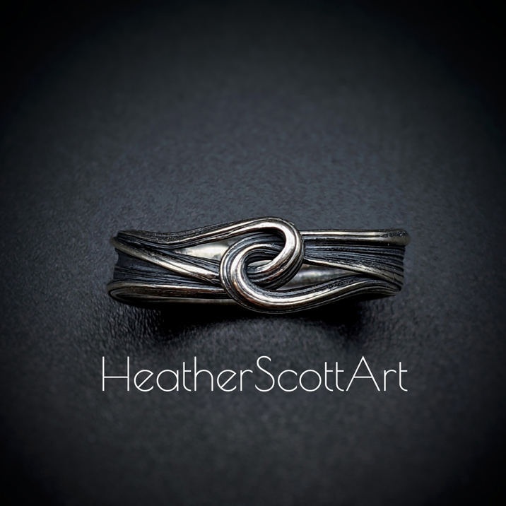 Sterling silver ring with a sculptural knot on the front. It has a linear texture that wraps around the entire ring.