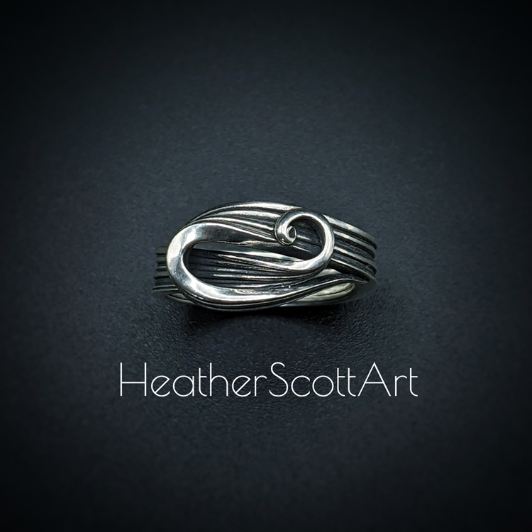 Sterling silver ring with a sculptural swirl on the front. It has a linear texture that wraps around the entire ring. The ring is sitting against a black background with the words Heather Scott Art in the foreground.