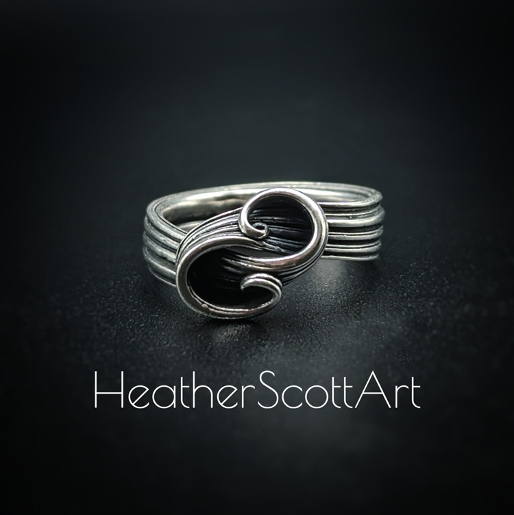 Sterling silver ring with a sculptural double swirl on the front. It has a linear texture that wraps around the entire ring. The ring is sitting against a black background with the words Heather Scott Art in the foreground.