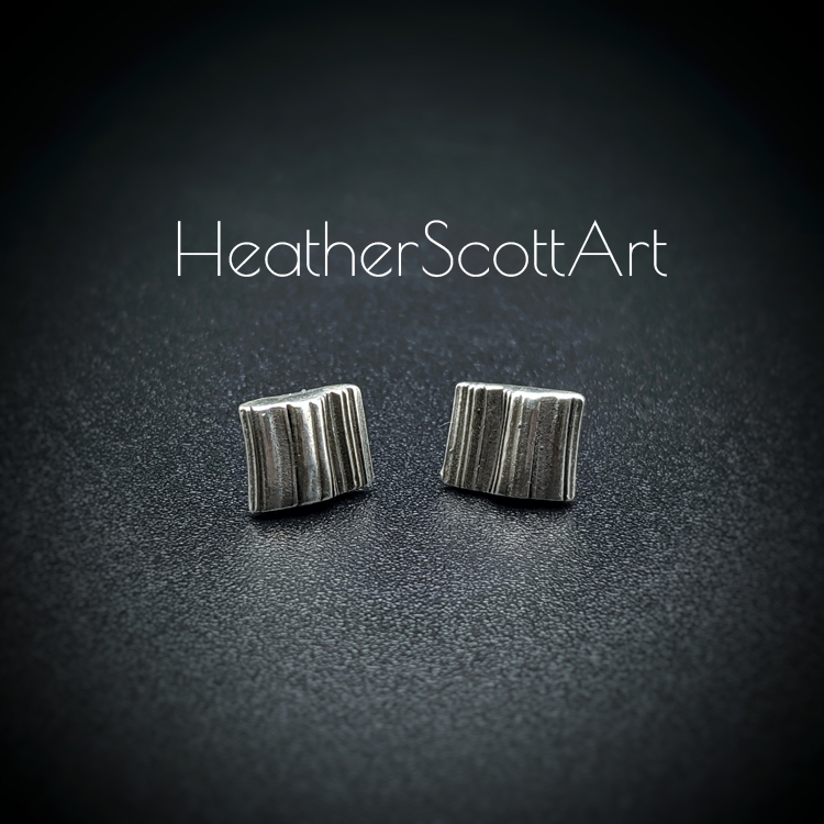 A pair of small rectangle stud earrings with a linear texture design in black and silver. They sit on a black background with the words Heather Scott Art above them.