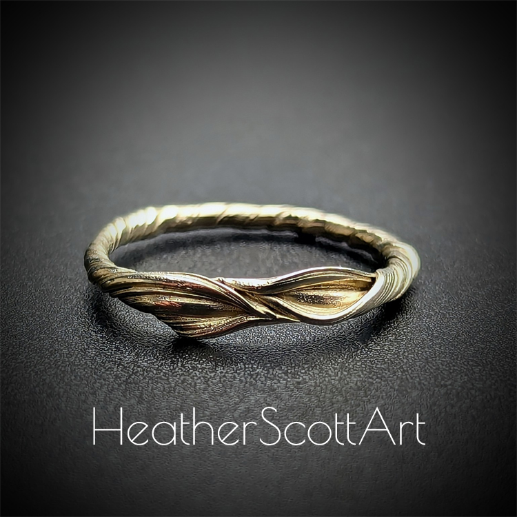 A 14k gold ring band ring featuring a leaf design in the front and a twisting vine texture band, displayed on a dark background.