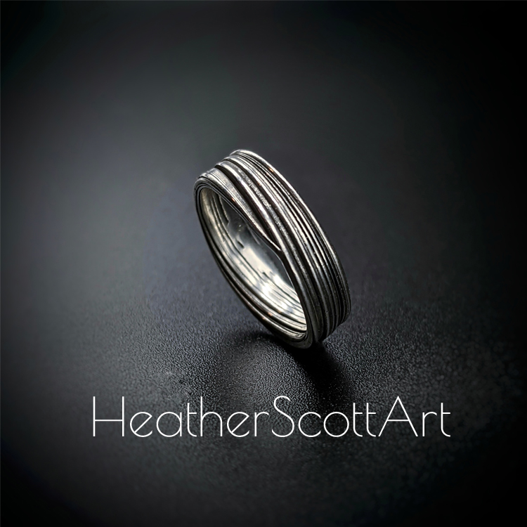 Handcrafted sterling silver band ring featuring flowing Mitsuro linear textures with a contrast finish, displayed on a dark background.