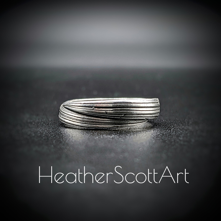 The front of a handcrafted sterling silver band ring featuring flowing Mitsuro linear textures with a contrast finish, displayed on a dark background.