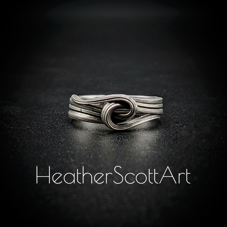 Close-up of a handcrafted knot ring with a linear texture, flowing design, created using the Mitsuro technique, displayed on a dark background.