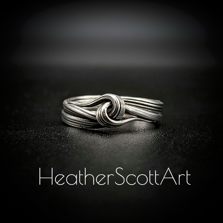 Close-up of a handcrafted knot ring with a linear texture, flowing design, created using the Mitsuro technique, displayed on a dark background.