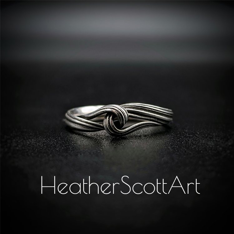 Close-up of a handcrafted knot ring with a linear texture, flowing design, created using the Mitsuro technique, displayed on a dark background.