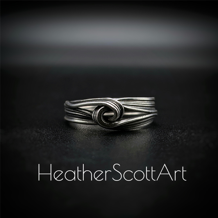 Close-up of a handcrafted knot ring with a linear texture, flowing design, created using the Mitsuro technique, displayed on a dark background.