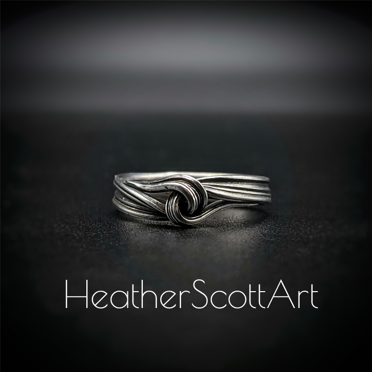 Close-up of a handcrafted knot ring with a linear texture, flowing design, created using the Mitsuro technique, displayed on a dark background.