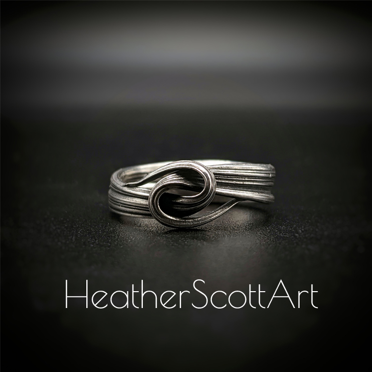 Close-up of a handcrafted knot ring with a linear texture, flowing design, created using the Mitsuro technique, displayed on a dark background.