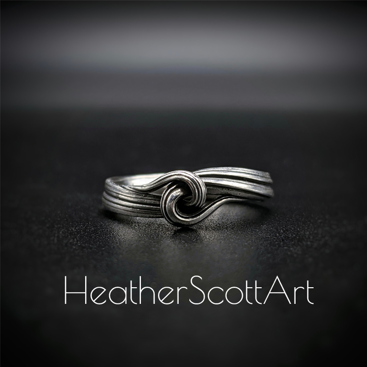 Close-up of a handcrafted knot ring with a linear texture, flowing design, created using the Mitsuro technique, displayed on a dark background.