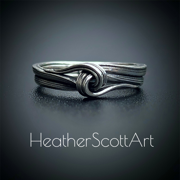 Close-up of a handcrafted knot ring with a linear texture, flowing design, created using the Mitsuro technique, displayed on a dark background.