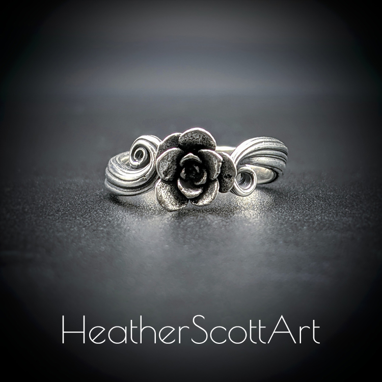 A handcrafted sterling silver ring featuring a detailed succulent flower at the center, set on a flowing Mitsuro-inspired band with intricate textures. The ring is displayed on a dark background, highlighting its elegant design and craftsmanship.