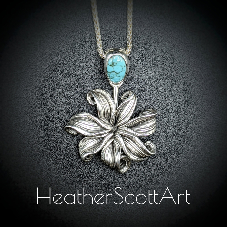 Handcrafted sterling silver pendant featuring a flowing flower design created with the mitsuro technique. The bail is adorned with an oval turquoise stone, adding a vibrant pop of blue. The pendant hangs elegantly on a silver chain, displayed on a dark background.